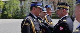 Zastępca komendanta głównego PSP przypina odznaczenie komendantowi szkoły, za którym stoją w szeregu inni strażacy