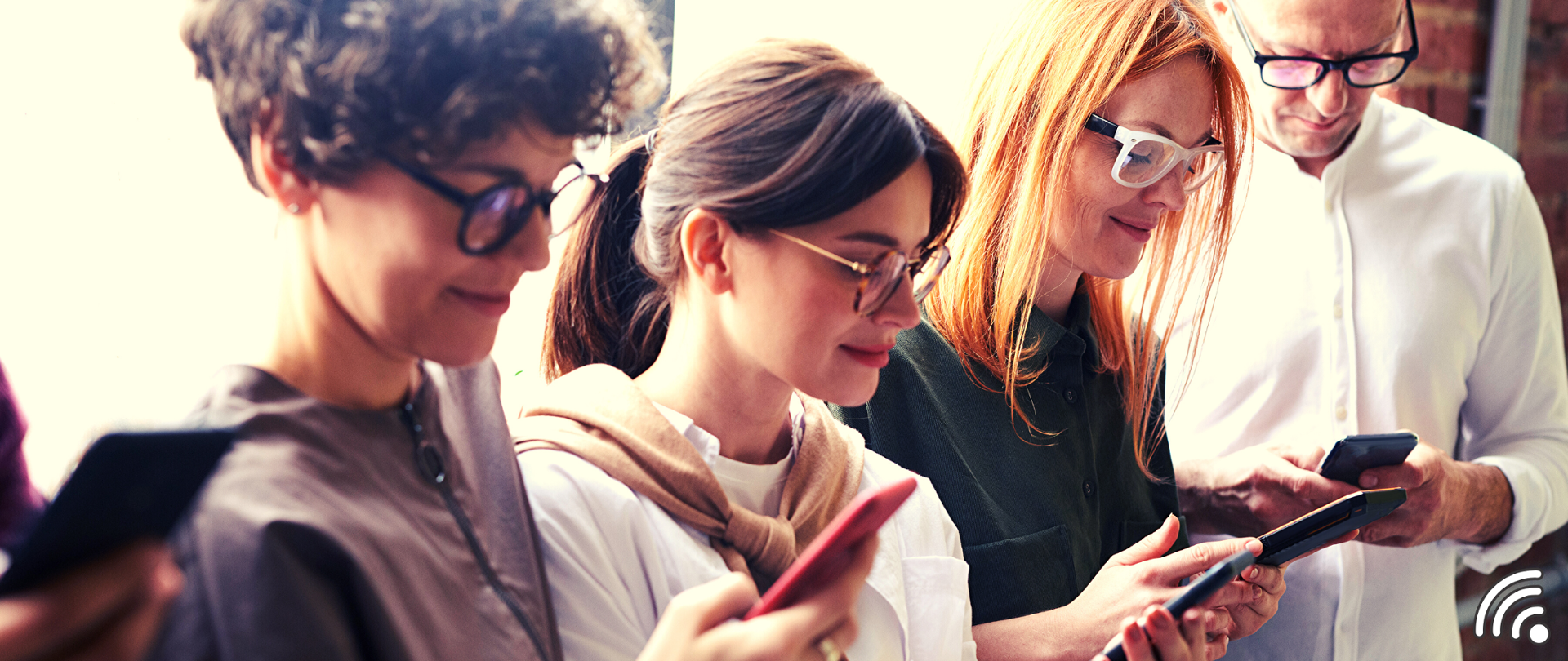 Trzy kobiety i jeden mężczyzna stoją w jednym rzędzie. Każda z osób patrzy w smartfon. Na obrazku znajduje się jeszcze symbol sieci WiFi.