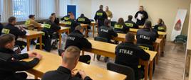 Zdjęcie przedstawia strażaków w trakcie egzaminu, w tle widoczna komisja egzaminacyjna