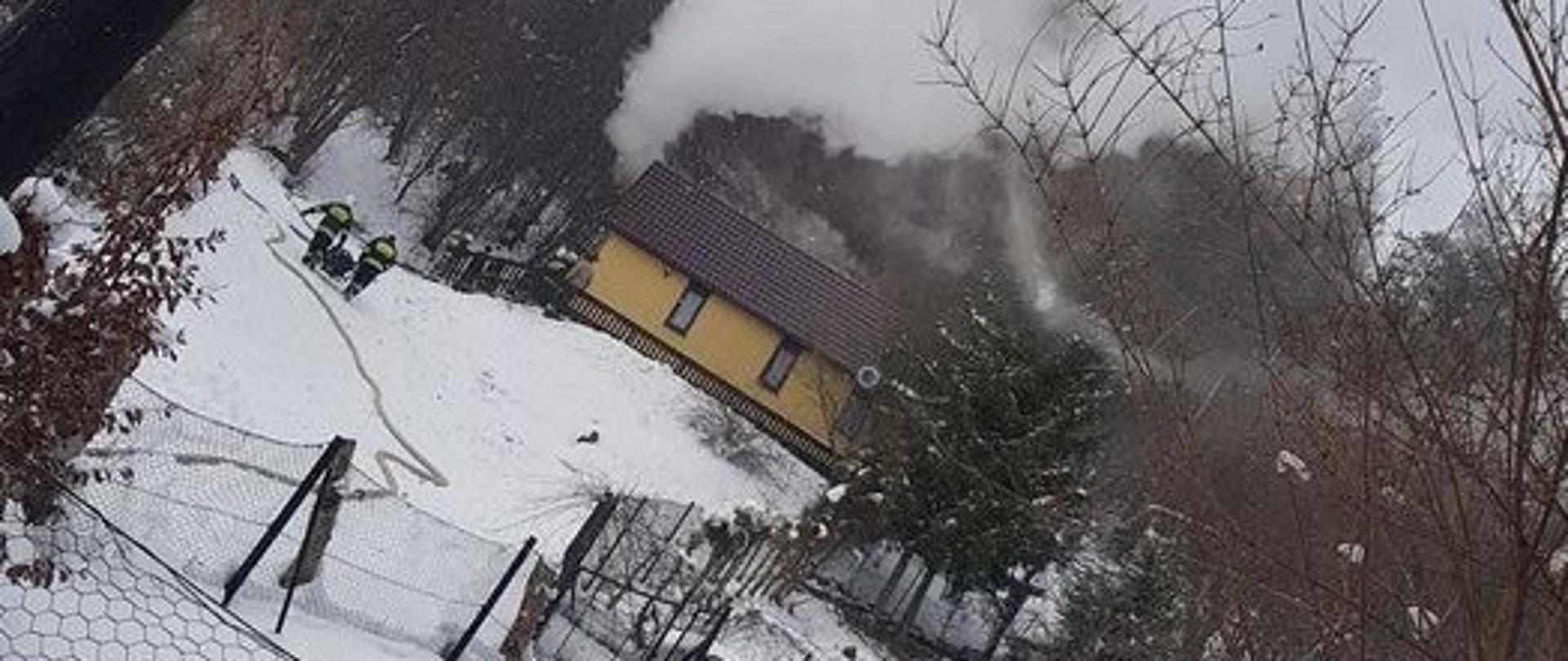 Wydobywający się dym z poddasza budynku. Strażacy przystępują do gaszenia. 