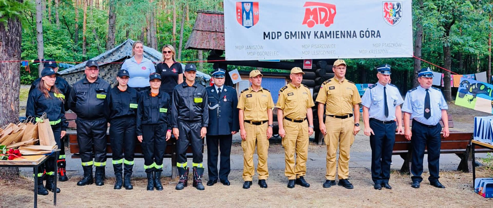 Strażacy oraz druhowie stojący na apelu w lesie.