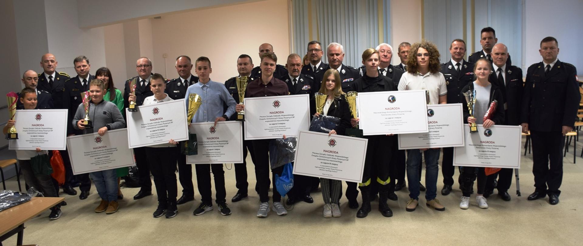 Laureaci konkursu z nagrodami na tle komisji sędziowskiej i opiekunów.