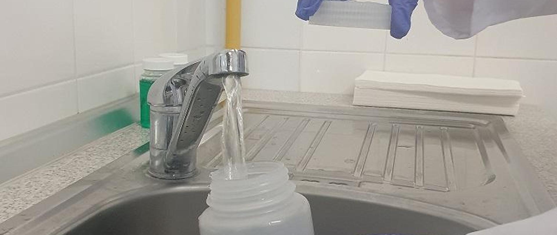 pobieranie próbki wody do badań laboratoryjnych. Osoba w jednorazowych rękawicach nalewa z kranu wodę do probówki