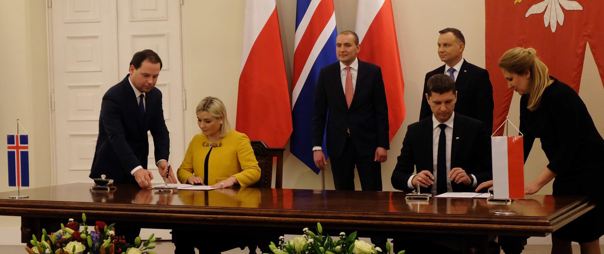 Polski minister edukacji wspólnie z islandzką minister edukacji podpisują deklarację. Za nimi stoją prezydenci obu krajów. W tle flagi Polski i Islandii. 