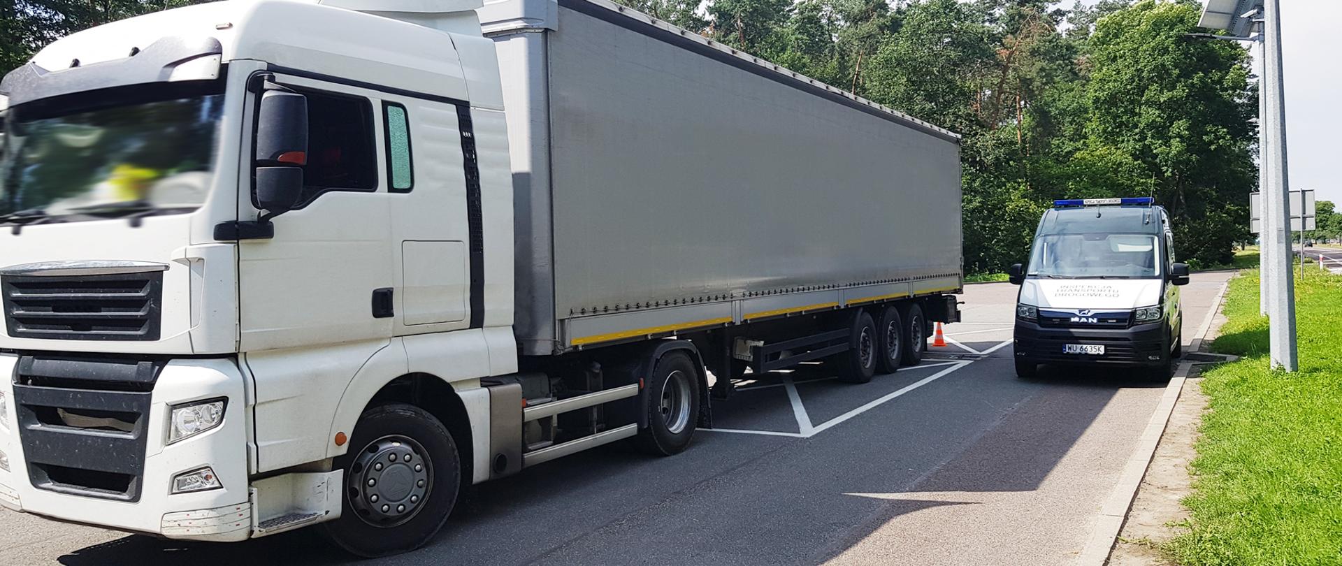 Ciężarówka zatrzymana do kontroli przez inspektorów lubelskiej Inspekcji Transportu Drogowego. Po lewej skontrolowany zespół pojazdów, po prawej inspekcyjny furgon. W tle, po prawej, ruch na drodze krajowej.