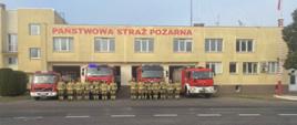 Strażacy stojąc na baczność na tle samochodów gaśniczych oddają cześć poległym strażakom z Ukrainy.