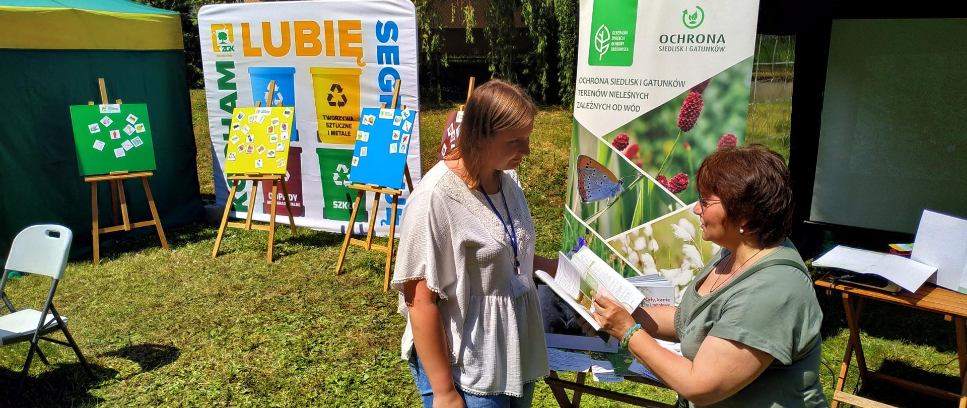 Dwie kobiety rozmawiają ze sobą, jedna trzyma w rękach książkę.