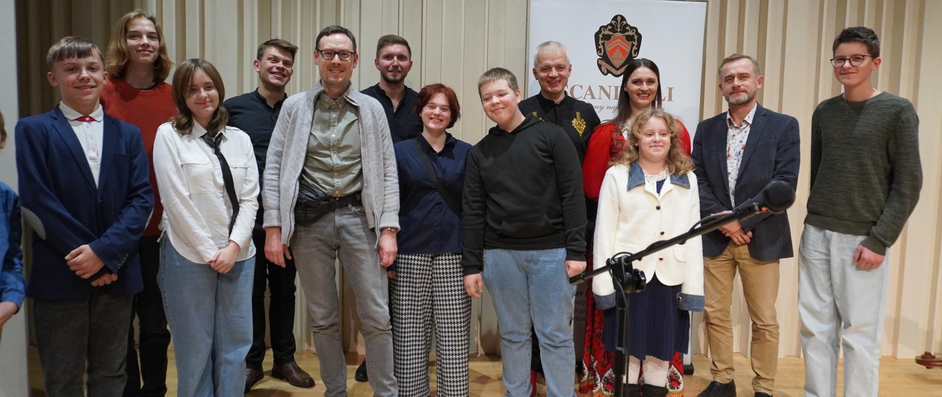 Do zdjęcia pozują na sali koncertowej kościerskiej szkoły muzycznej członkowie zespołu "Tekla Klebetnica" oraz uczniowie i nauczyciele klasy akordeonu z wejherowskiej szkoły muzycznej. Wszyscy się uśmiechają patrząc w obiektyw.