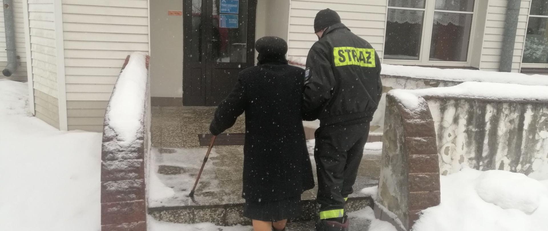 Strażak OSP Krynki pomaga przejść do punktu szczepień starszej kobiecie