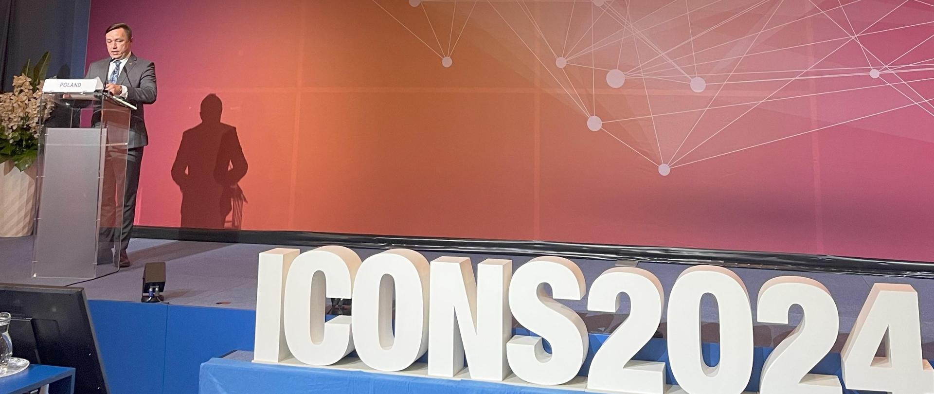  Prezes Państwowej Agencji Atomistyki podczas konferencji ICONS 2024 wypowiada się na scenie obok napisu ICONS2024 na kolorowym tle z logo IAEA