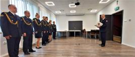 Sala konferencyjna KM PSP w Świnoujściu. Komendant Miejski odczytuję decyzję przed frontem szyku ośmiu funkcjonariuszy. Wszyscy strażacy w szeregu w mundurach wyjściowych ze sznurem.