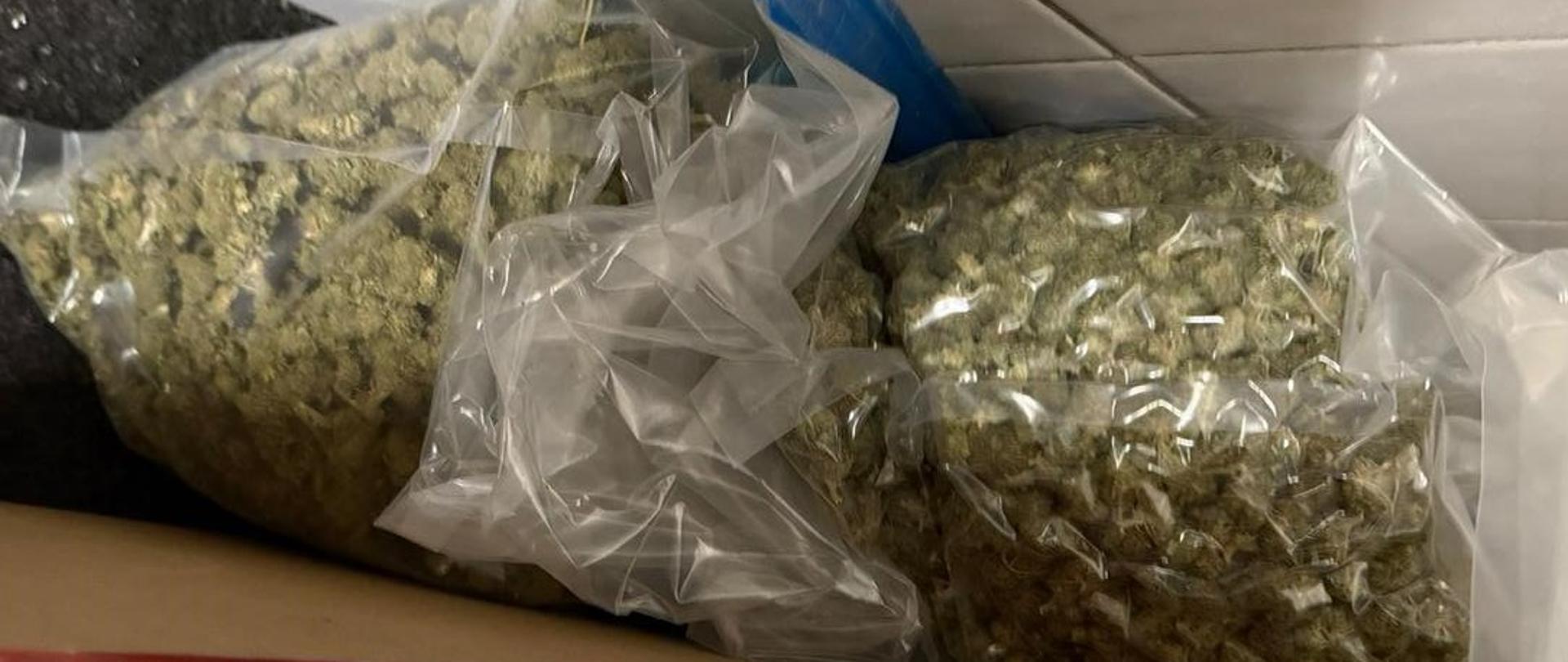 Przy ścianie z białych płytek leżą przezroczyste worki foliowe zawierające narkotyki.