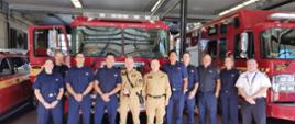 Komendant główny PSP, zastępca dyrektora Biura Komendanta Głównego PSP oraz 9 strażaków kanadyjskich na grupowym zdjęciu na tle 3 samochodów straży pożarnej
