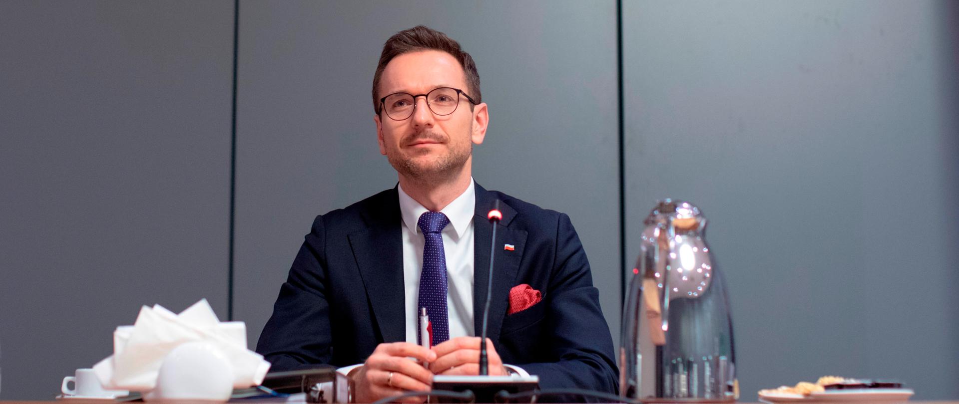Wiceminister Waldemar Buda siedzi przy stole konferencyjnym. Na jego blacie mikrofon, czajnik i naczynia.