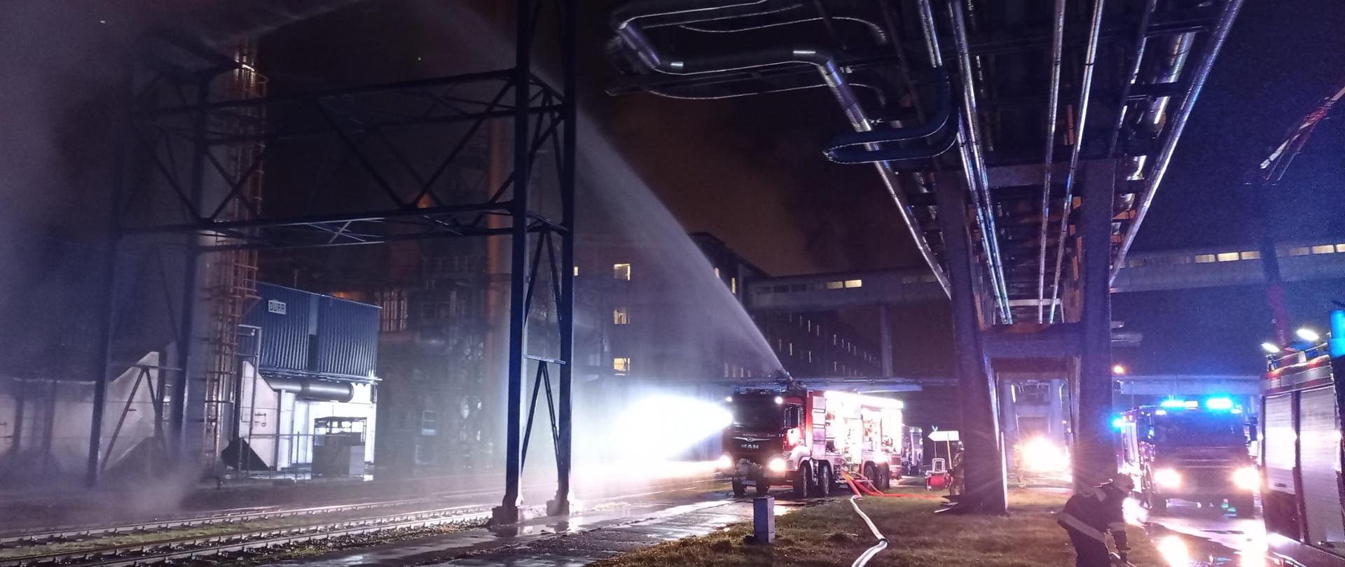 Samochód gaśniczy podaje wodę z działka gaśniczego, w tle widoczne budynki zakładu