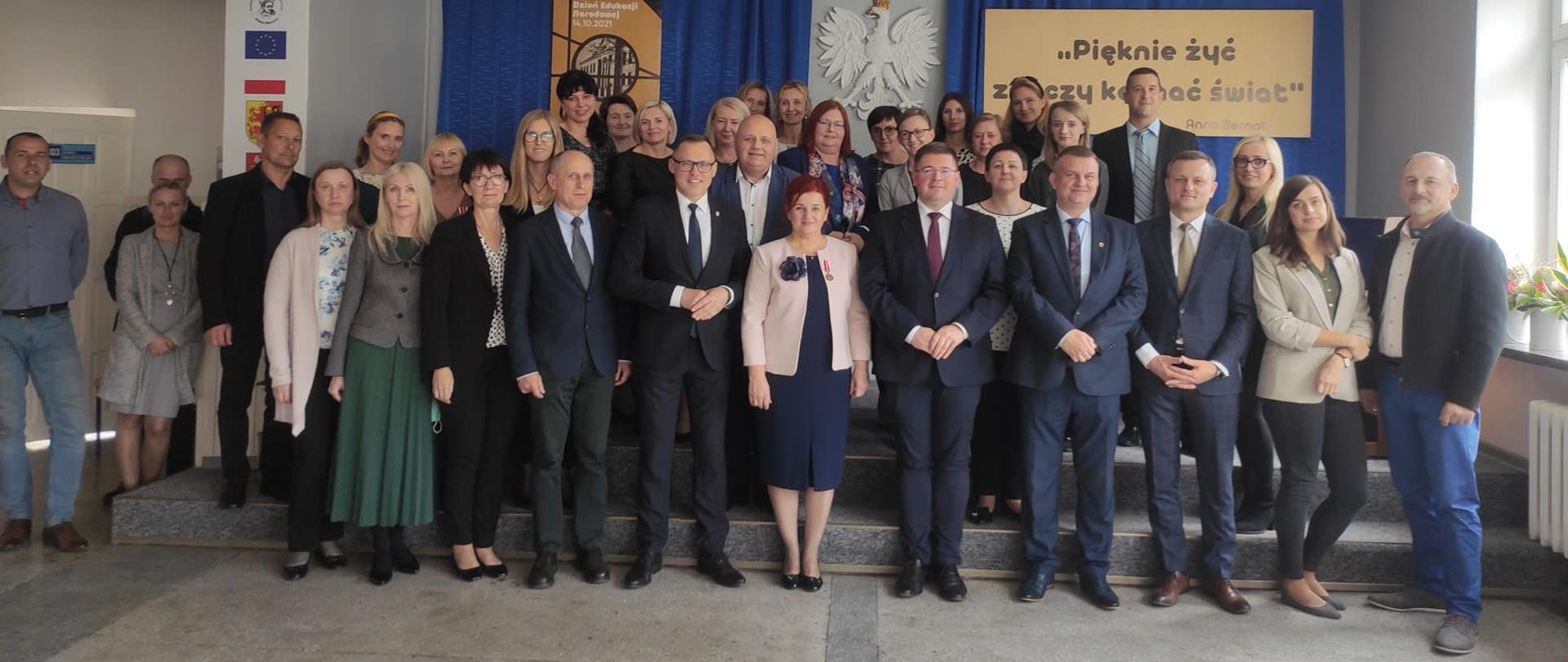 Dzień Edukacji Narodowej w Jagiellończyku z udziałem wiceministra Tomasza Rzymkowskiego. Zdjecie grupowe przedstawia wiceministra Rzymkowskiego wraz z nauczycielami szkoły 