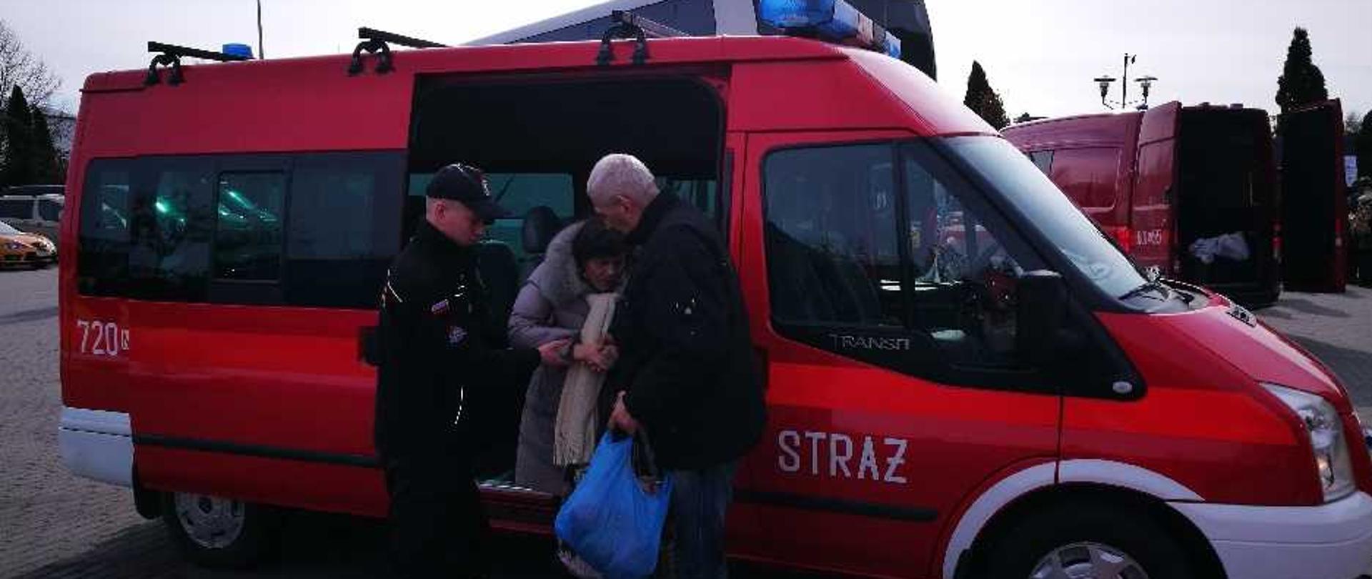 Strażak pomaga kobiecie i mężczyźnie z Ukrainy wysiąść z samochodu strażackiego.
