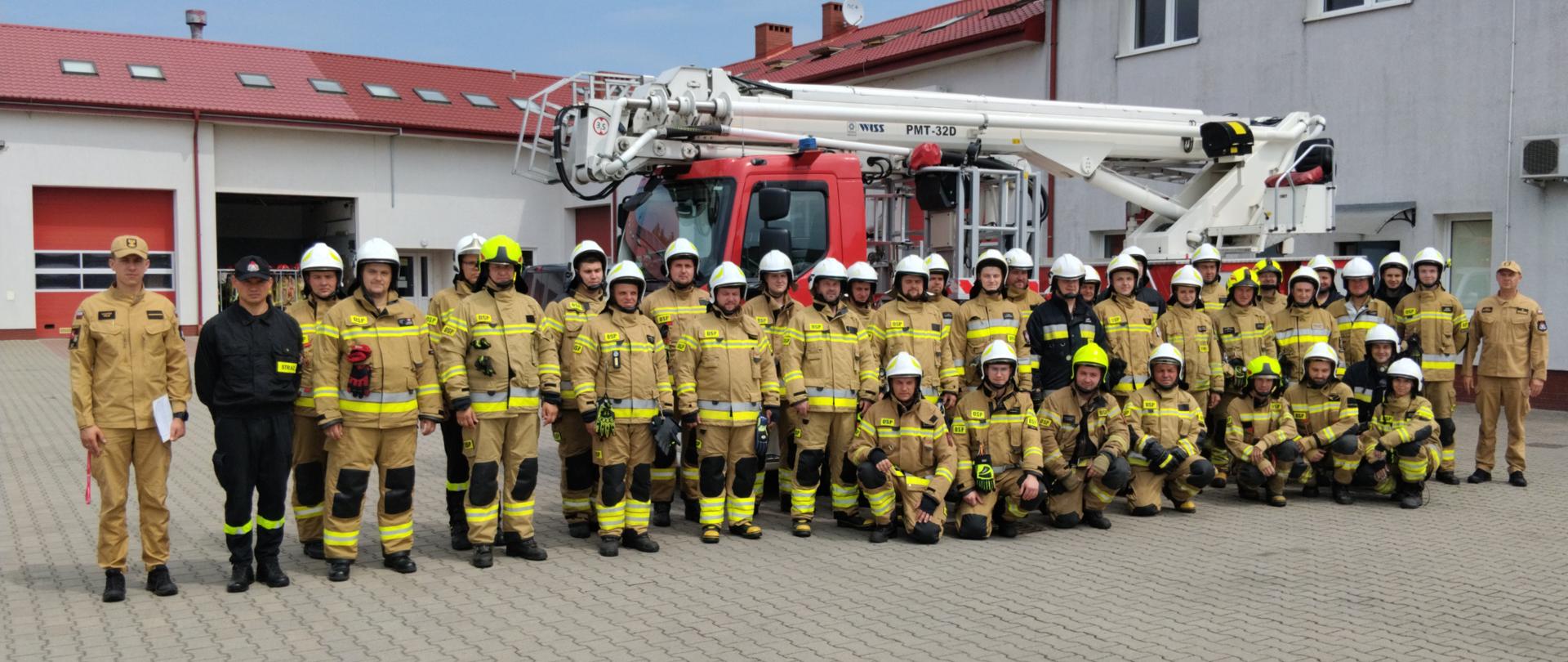 Zdjęcie przedstawia grupę strażaków OSP stojących przed samochodzie pożarniczym typu podnośnik.