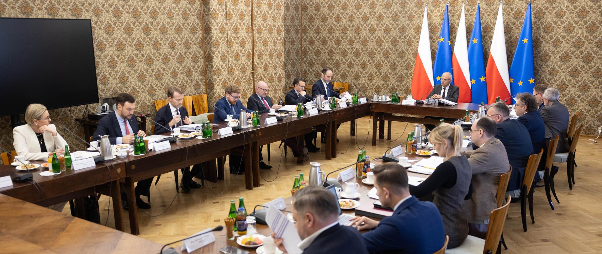 Szeroki kadr. Uczestnicy posiedzenia Zespołu do spraw Programowania Prac Rządu, podczas obrad, siedzą przy stołach ustawionych w kształt prostokąta. U szczytu stołu widoczny przewodniczący Zespołu, Sekretarz Stanu, Zastępca Szefa Kancelarii Prezesa Rady Ministrów Grzegorz Karpiński. Po lewej stronie Sekretarz Stanu, Wiceprzewodnicząca Komitetu ds. Pożytku Publicznego Adriana Porowska. Fot. Stefan Maszewski