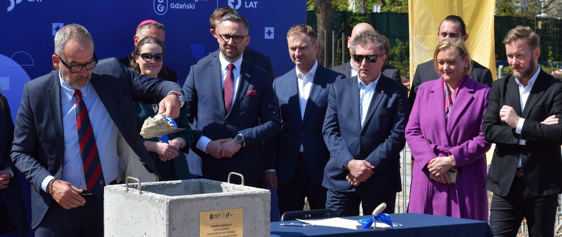 kilka osób stoi i patrzy na wmurowanie kamienia węgielnego pod budowę centrum sportowego
