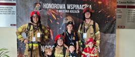 Zdjęcie przedstawia strażaków w ubraniach specjalnych pozujących na plakacie honorowej wspinaczki 