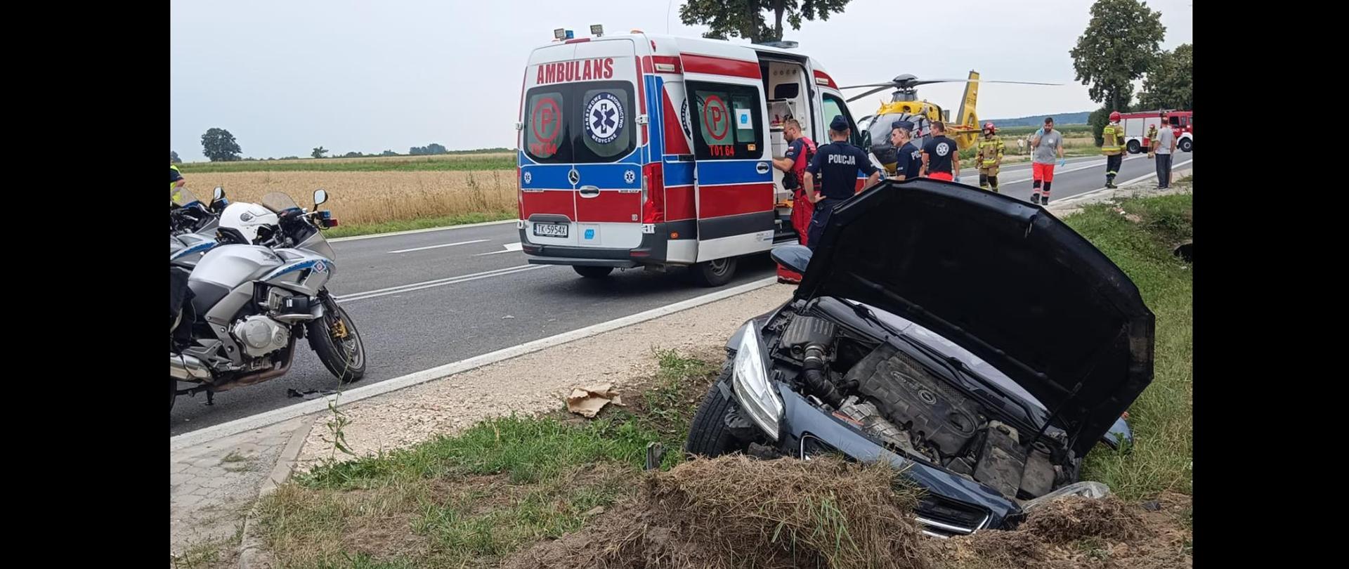 Zdjęcie przedstawia samochód osobowy w rowie. W tle samochody gaśnicze, LPR i karetka pogotowia.