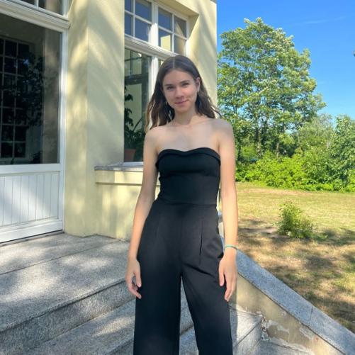 Zdjęcie kolorowe. Nastolatka w czarnym stroju stoi na schodach. W tle zielona roślinność.