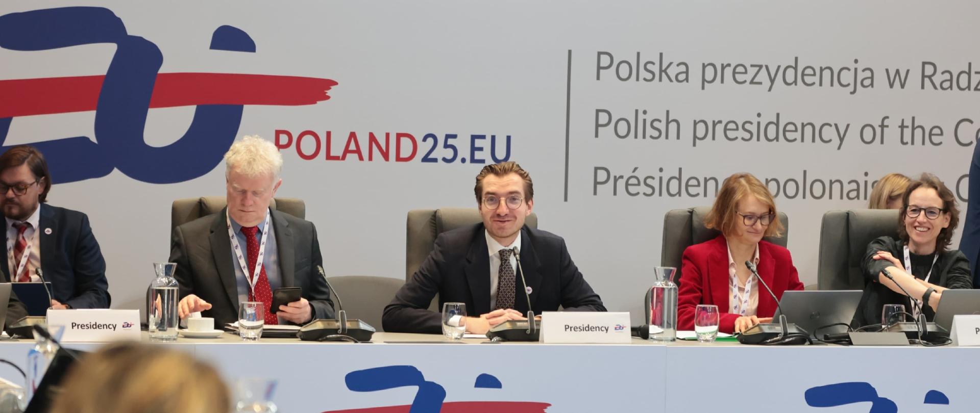 Grupa osób w sali konferencyjnej siedzi przy stołach. Trzeci od lewej wiceminister Jan Szyszko.