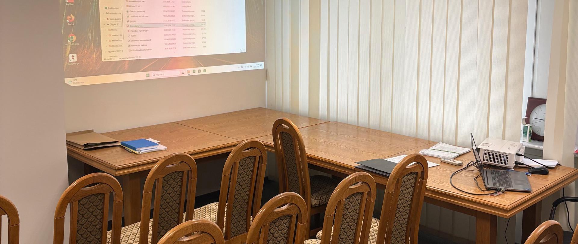 Przestrzeń konferencyjna z ustawionymi krzesłami i ekranem do prezentacji.