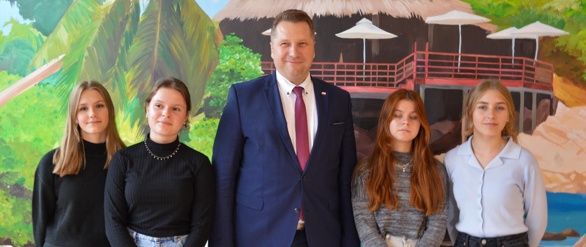 Minister wśród uczennic, z lewej strony ministra stoją dwie uczennice i z prawej dwie 