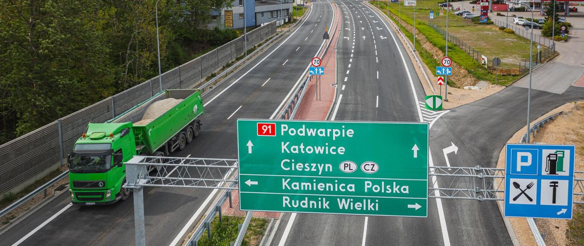 Odcinek drogi krajowej nr 91 w kierunku Podwarpia, Katowic i Cieszyna, z widocznymi znakami kierunkowymi, zatoką zjazdową na Kamienicę Polską i Rudnik Wielki oraz pojazdami ciężarowymi.