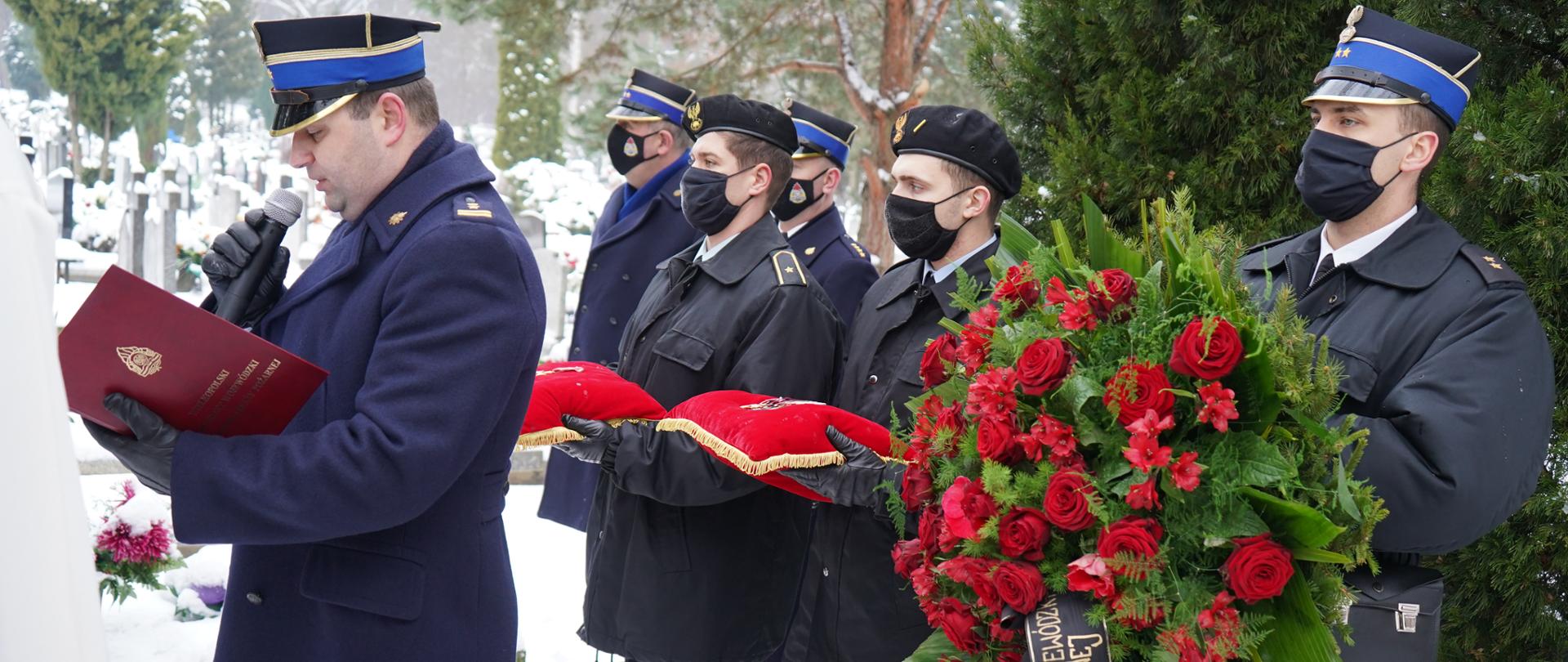 strażak w płaszczu czytajacy list , za nim stoi tzrech strażakó trzymajacych odznaczenia oraz wieniec