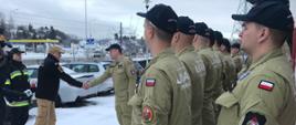 Dowódca grupy wita się z kierownictwem Komendy Wojewódzkiej Państwowej Straży Pożarnej w Gdańsku w rzędzie stoją strażacy w mundurach USAR Poland.