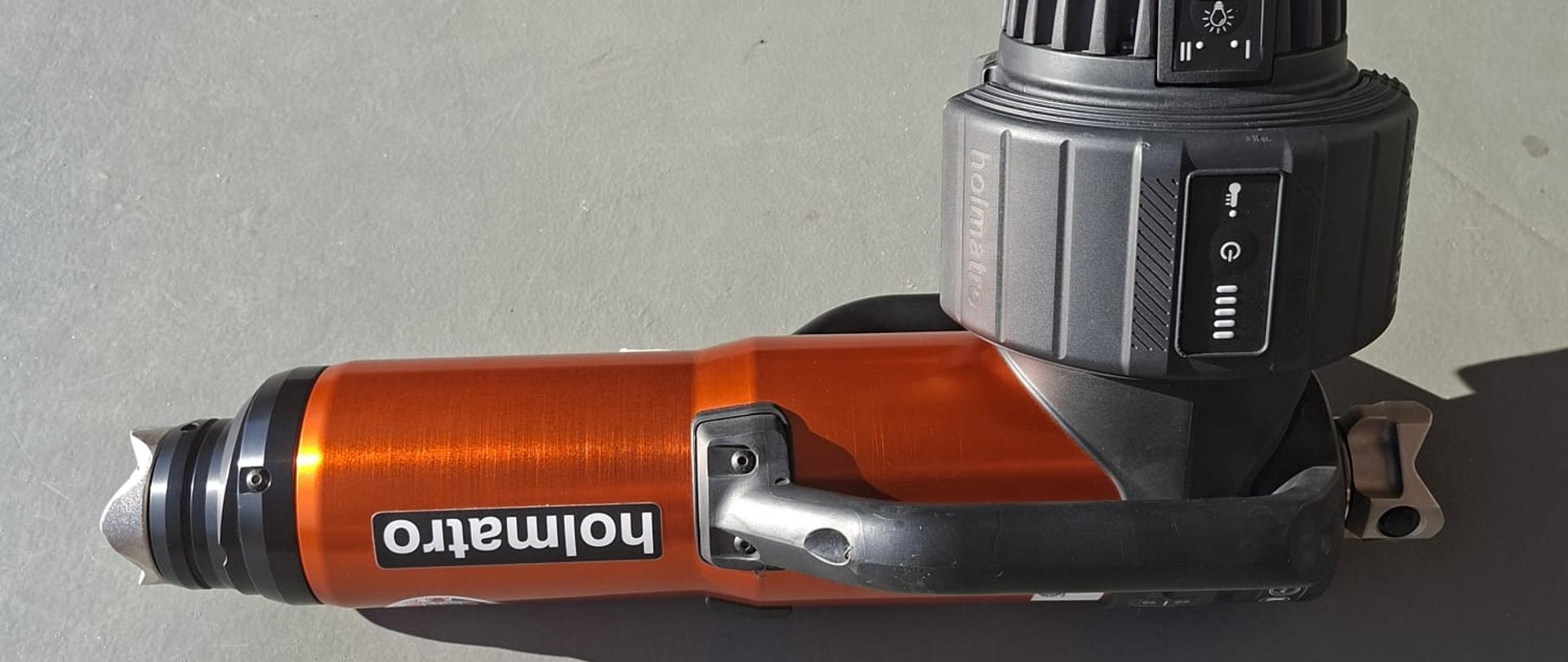 Zdjęcie przedstawia ratownicze urządzenie hydrauliczne z napędem elektrycznym (bateryjnym) w kolorze czerwono-czarnym