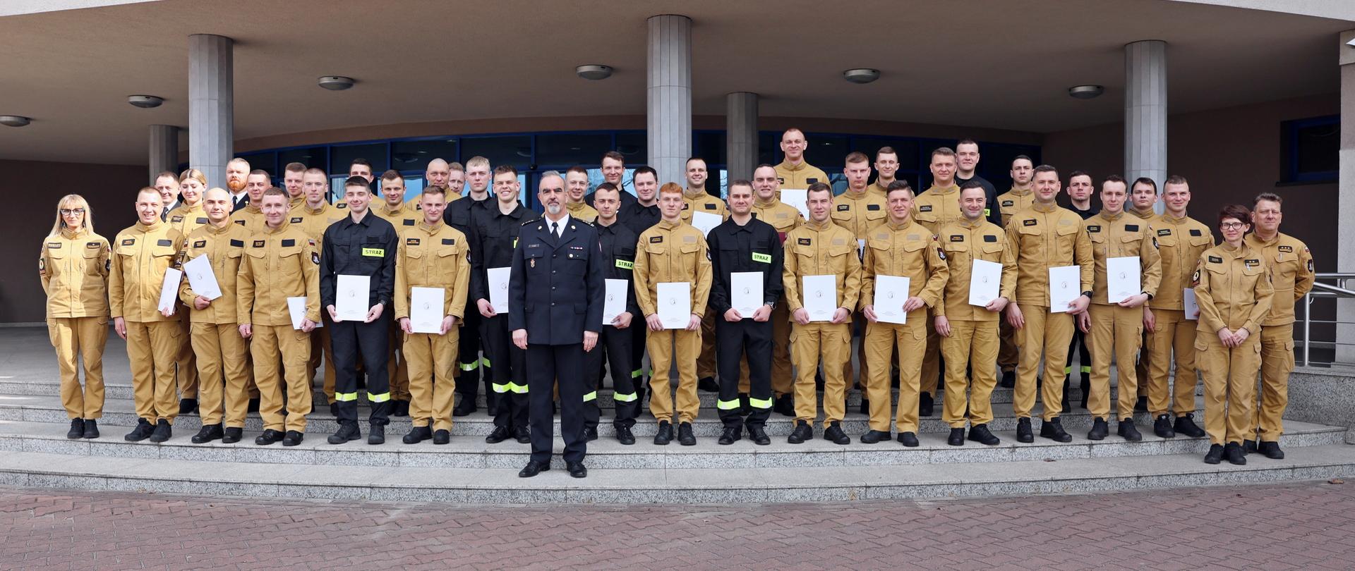 Pamiątkowe zdjęcie grupowe funkcjonariuszy PSP, którzy ukończyli szkolenie w towarzystwie Zastępcy Komendanta Centralnej Szkoły PSP oraz przedstawicieli kadry CS PSP