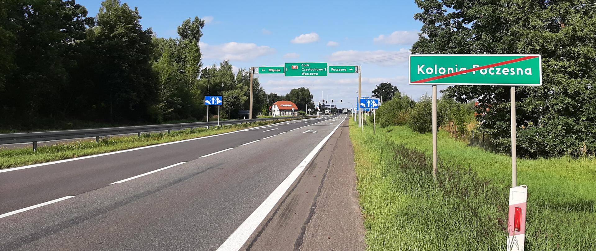 Fotografia dwuprzestrzennej drogi krajowej nr 91 na granicy Kolonii Poczesnej. Droga wyposażona jest w bariery ochronne oznakowanie pionowe i poziome. W tle widoczna sylabizacja świetlna. Droga otoczona jest zielenią przydrożną. 