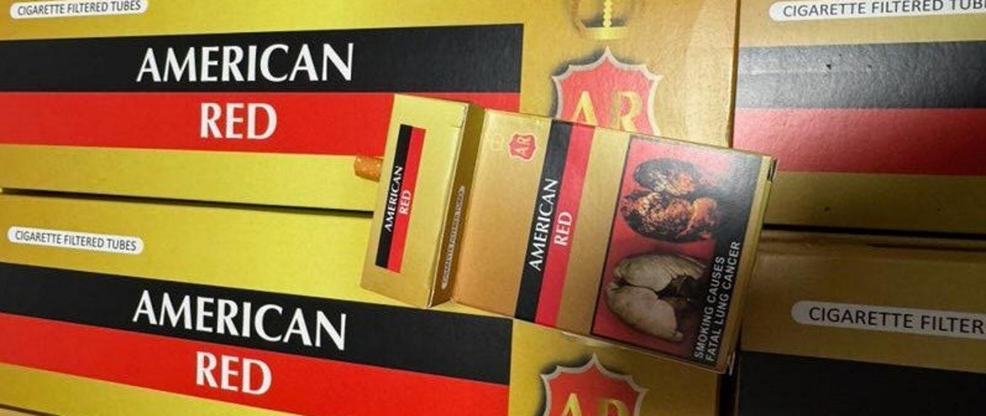 Kartony z papierosami, na nich leży otwarta paczka papierosów. 