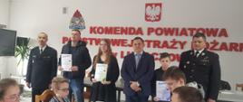 Zdjęcie przedstawia laureatów trzech pierwszych miejsc w każdej grupie wiekowej OTWP w 2022, wraz z przybyłymi gośćmi. Na ścianie napis Komenda Powiatowa Państwowej Straży Pożarnej w Lubaczowie