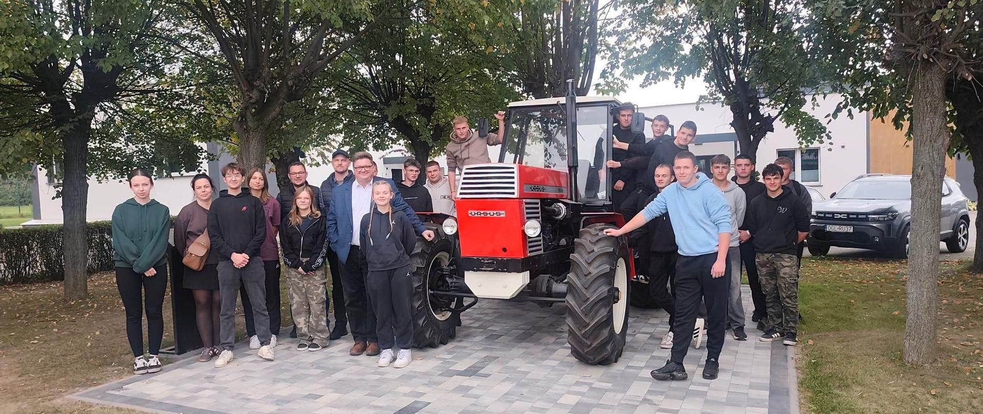 Grupa uczniów ZSCKR w Sichowie Dużym stoi przy czerwonym ciągniku rolniczym podczas wycieczki edukacyjnej do Kombinatu Rolnego Kietrz.