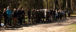 Na zbiórce stoją uczestnicy akcji "Wspólne sadzenie lasu". Wśród nich są przedstawiciele nadleśnictwa, straży pożarnej, policji i lokalnej ludności.