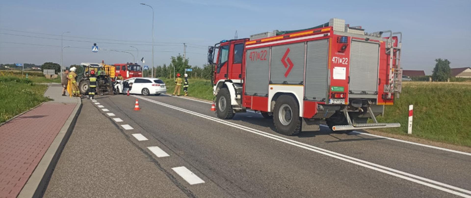 Jezdnia w tle samochody pożarnicze raz uszkodzony ciągnik z pojazdem osobowym