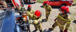 Strażacy w umundurowaniu specjalnym podczas ćwiczeń używają nożyc hydraulicznych do cięcia karoserii samochodu