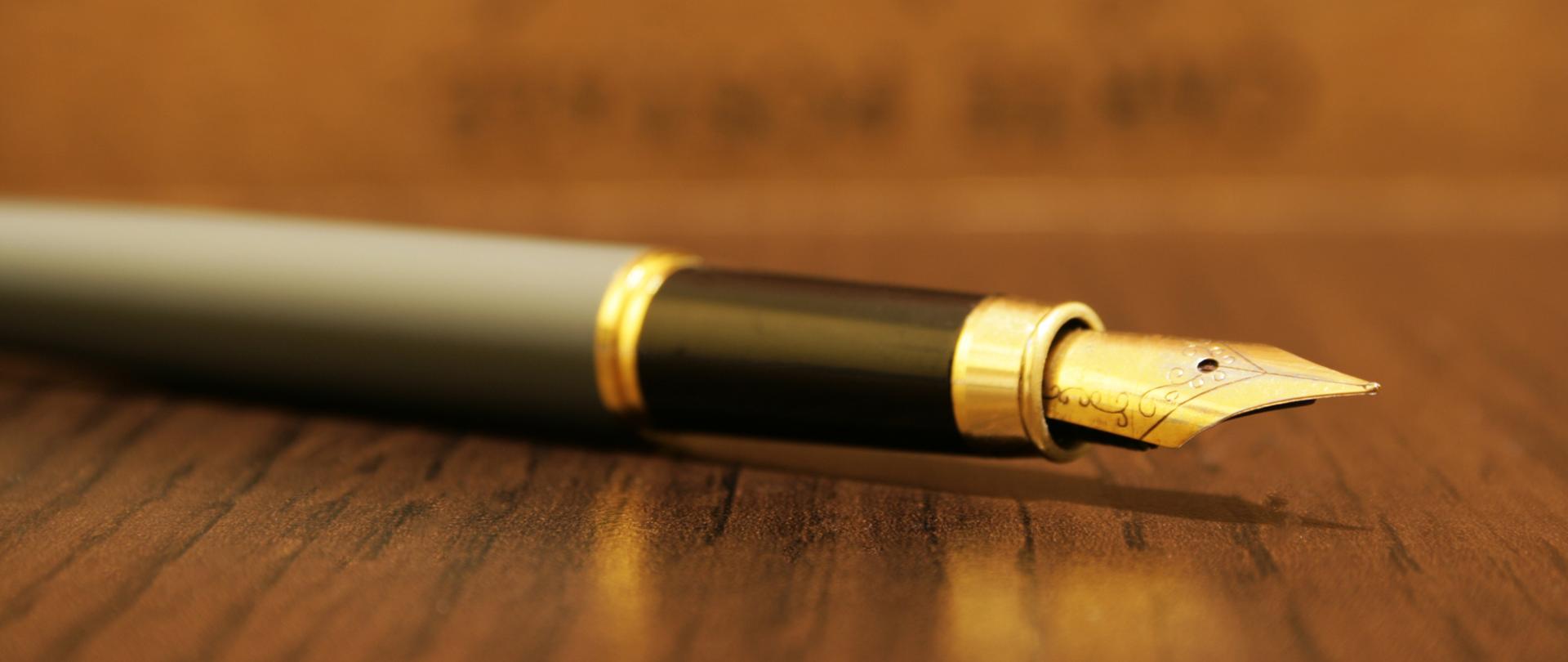 Złote pióro na drewnianym blacie.