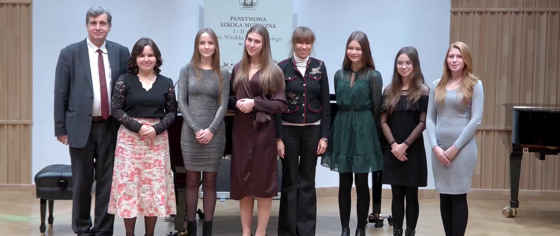 Zdjęcie. Estrada Sali Koncertowej PSM w Nysie. Stoją wykonawcy koncertu kolęd. Z tyłu w tle stoi baner PSM Nysa.