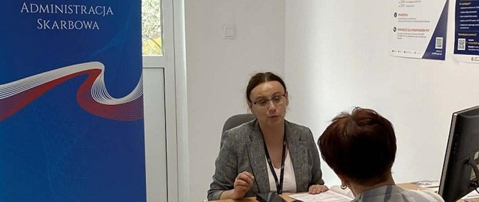 Przed ekspertką siedzi klientka. Na biurku leżą dokumenty. 