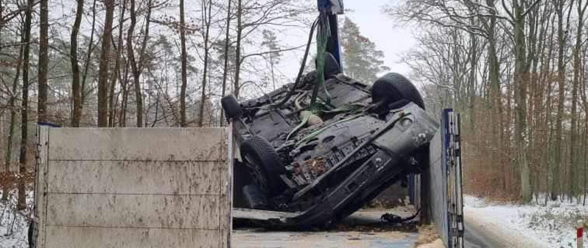 Na zdjęciu widać samochód osobowy po uprzednim dachowaniu znajdujący się na pace samochodu ciężarowego.