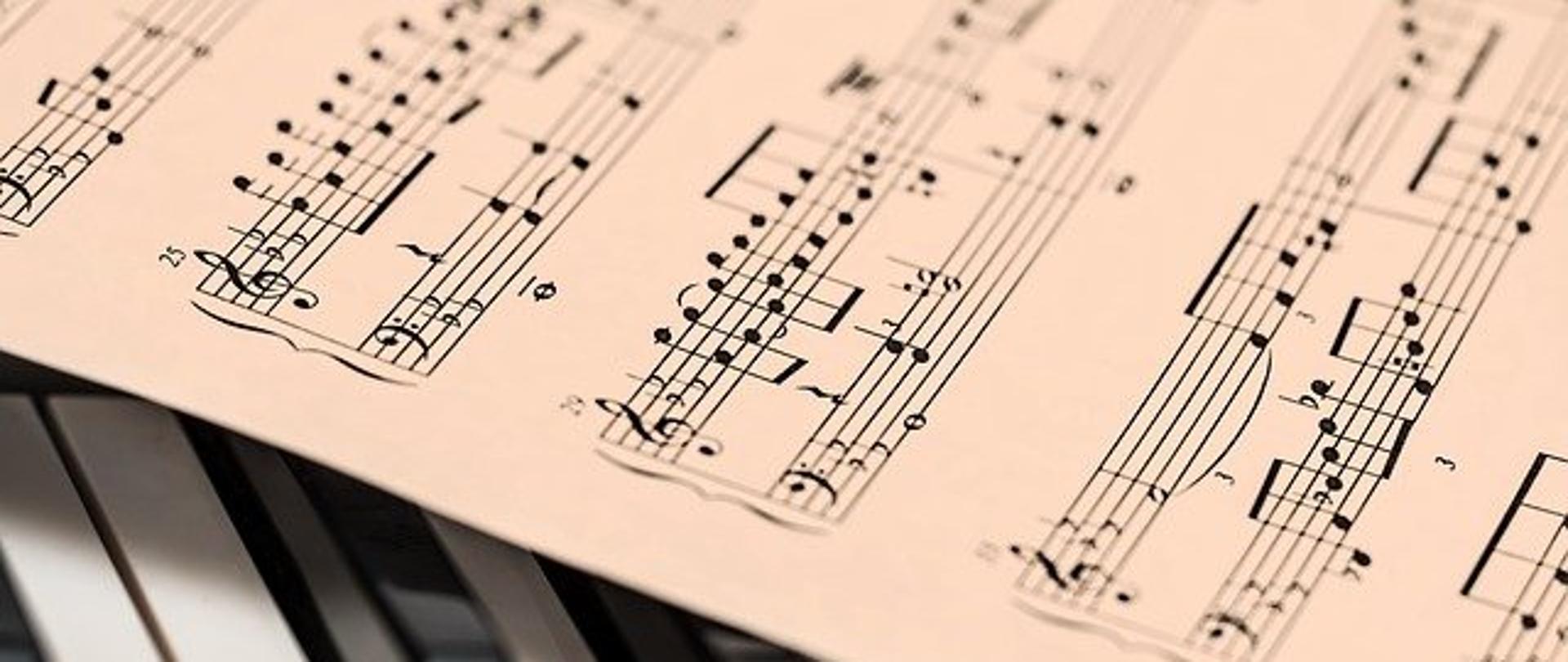 Zdjęcie przedstawia nuty położone na klawiaturze fortepianu