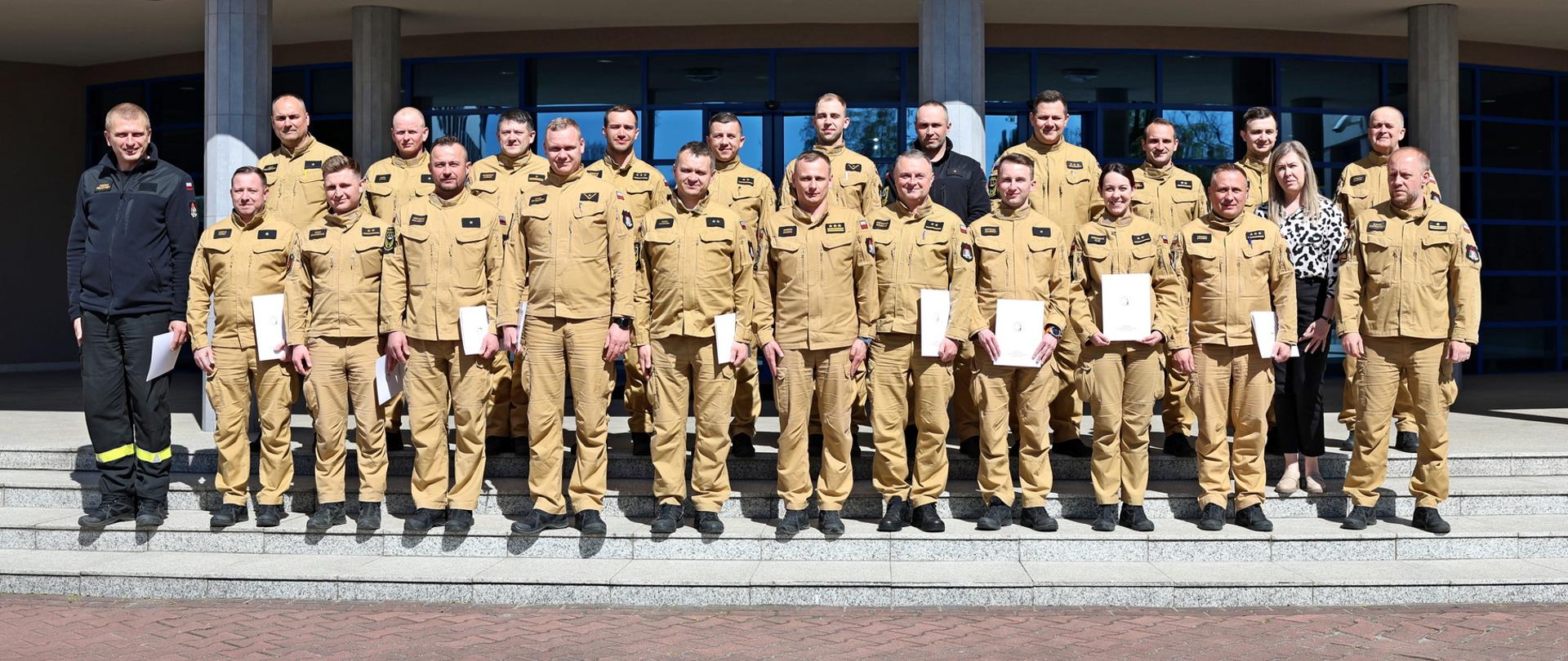 Pamiątkowe zdjęcie grupowe funkcjonariuszy PSP będących uczestnikami szkolenia z zakresu kierowania działaniami ratowniczymi na poziomie taktycznym (20 osób) w towarzystwie Zastępcy Komendanta Centralnej Szkoły PSP, kobiety oraz dwóch funkcjonariuszy CS PSP