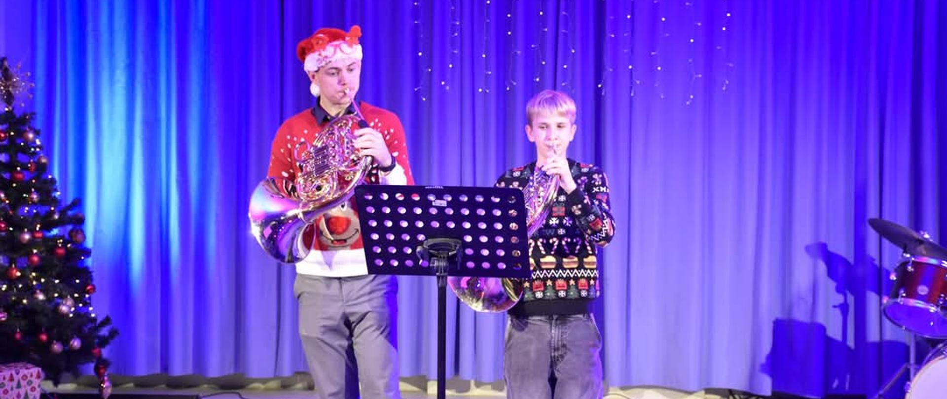 na tle choinki dwaj uczniowie grający na tubach