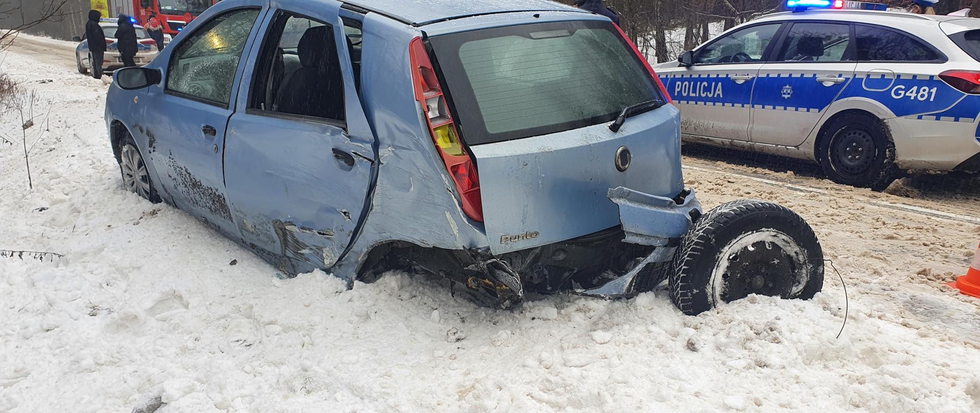 Samochód osobowy koloru jasno niebieskiego, w tle po prawej radiowóz policji w tle po lewej radiowóz oraz wóz straży pożarnej